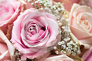 A coloured macro photo of a detailed bouquet with pink roses, white small flowers and a fake diamond in the centre of the rose