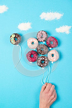 Coloured mini donuts on blue background, creative food idea, hand holding donuts in a shape of balloons in the sky with clouds