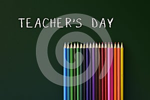Coloured pencils and text teachers day written in a green chalkb