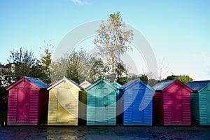 Colourful Beach Huts in a row under a blue sky.