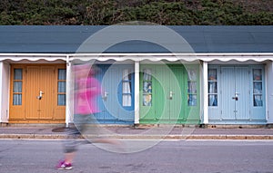 Colourful beach huts with runner in front, located on the promenade on the Bournemouth UK sea front.