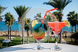 Colourful cold Rainbow Paradise and Strawberry daiquiri cocktail drinks served in glasses at pool bar overlooking blue pool, sea
