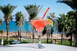 Colourful cold Strawberry daiquiri cocktail drink served in glass at outdoor cafe overlooking blue sea and palm trees, relax and