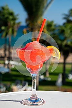 Colourful cold Strawberry daiquiri cocktail drink served in glass at outdoor cafe overlooking blue sea and palm trees, relax and