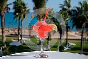 Colourful cold Strawberry daiquiri cocktail drink served in glass at outdoor cafe overlooking blue sea and palm trees, relax and
