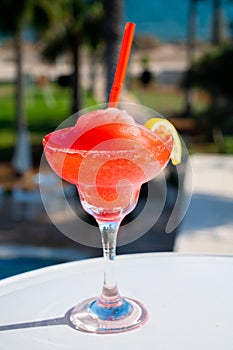 Colourful cold Strawberry daiquiri cocktail drink served in glass at outdoor cafe overlooking blue sea and palm trees, relax and