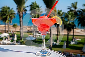 Colourful cold Strawberry daiquiri cocktail drink served in glass at pool bar overlooking blue pool, sea and palm trees, relax and