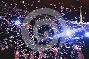 Colourful confetti explosion fired on dance floor air during a concert festival, crowded concert hall with scene stage lights,