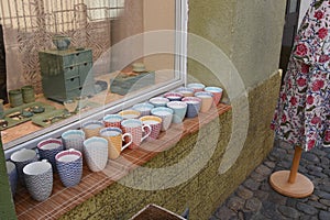 Colourful cups and mugs exposed for sale in window-sill of the small corner shop