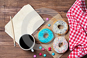 Colourful donuts, cup of coffee, smarties and old blank paper sheet with pencil on wooden table, top view