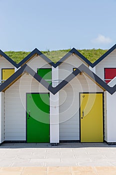 Colourful doors of yellow and green, with each one being numbered individually, of white beach houses on a sunny day