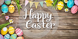 Colourful Easter background with Happy Easter Text decorated eggs and spring flowers, on a rustic wooden background