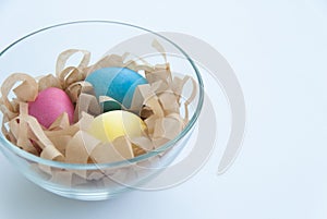 Colourful Easter eggs on a hay in a glass bowl. Isolated on white background. Close up