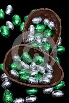 Colourful foil wrapped chocolate easter eggs in silver, and green with two halves of a large brown milk chocolate egg.