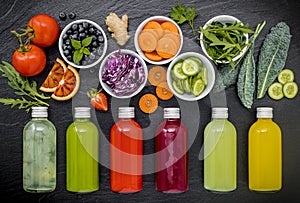 Colourful healthy smoothies and juices in bottles with fresh tropical fruit and superfoods on dark stone background with copy