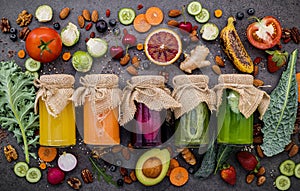 Colourful healthy smoothies and juices in bottles with fresh tropical fruit and superfoods on dark stone background with copy