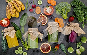 Colourful healthy smoothies and juices in bottles with fresh tropical fruit and superfoods on dark stone background with copy