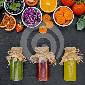 Colourful healthy smoothies and juices in bottles with fresh tropical fruit and superfoods on dark stone background with copy