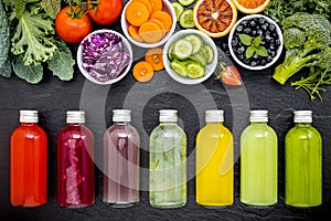 Colourful healthy smoothies and juices in bottles with fresh tropical fruit and superfoods on dark stone background with copy