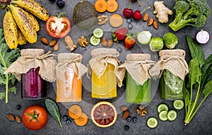 Colourful healthy smoothies and juices in bottles with fresh tropical fruit and superfoods on dark stone background with copy