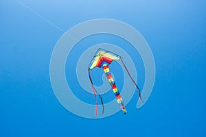 A colourful kite flying in a clear blue sky with a long tail and streamers