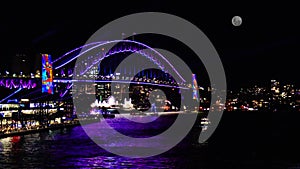 Colourful Light show at night on Sydney Harbour NSW Australia full moon rising above the Bridge