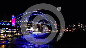 Colourful Light show at night on Sydney Harbour NSW Australia full moon rising above the Bridge