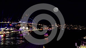 Colourful Light show at night on Sydney Harbour NSW Australia full moon rising above the Bridge