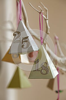 Colourful paper party decorations with the numbers eighteen and 25 with a silver finish, hanging on an painted white branch