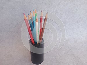 Colourful pencils stacked in a black wooden holder. Grey and white background.