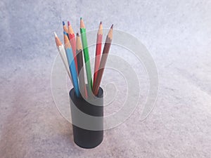 Colourful pencils stacked in a black wooden holder. Grey and white background.