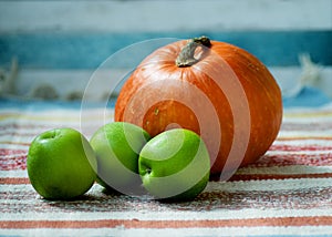 Colourful pumpkin and three green apples on the indian rug.