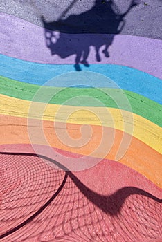 Colourful rainbow rubber floor on an outdoor amusement park with a strong shadow of a playing seat casted.