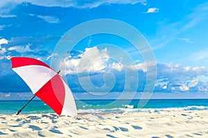 Colourful red and white umbrella on the ocean beach with beautiful blue sky and clouds. Relaxation, vacation idyllic background