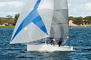 Colourful sailing dingy with blue and white spinnaker being navigated by junior sailors