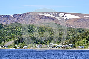 Colourful seaside village along Bonne Bay with snow packs on The Tablelands
