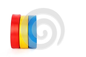 Colourful shiny satin ribbons in a rolls on a white background