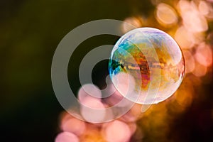 Colourful soap bubble floating against a mainly dark background with a streak of light bubble bokeh. photo