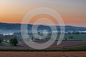 Colourful sunrise on a summer morning with a little fog on the ground and spectacular views over the Dutch hillside in Limburg