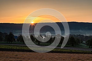 Colourful sunrise on a summer morning with a little fog on the ground and spectacular views over the Dutch hillside in Limburg