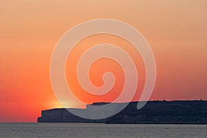 A colourful sunset over the cliffs of Paradis bay in Malta with a view on the Island of Gozo in the Mediterranean Sea