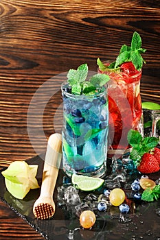 Colourful sweet cocktails with mint, lime, ice, berries on the wooden background. Refreshing summer beverages. Copy space.