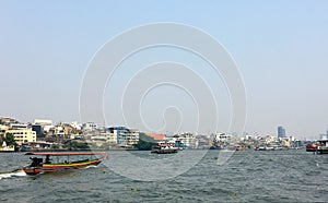 Colourful Thai long-tail sightseeing boat on the Chao Phraya River with cityscape background in windy and cloudy day