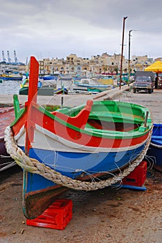 A colourful traditional Maltese fishing boat Luzzu on display with old houses behind at cloudy fishing village Marsaxlokk, Malta