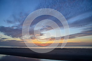 A colourful tropical orange coloured nimbostratus cloud coastal sunrise seascape in a blue sky. Thailand