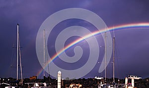 Colourful vivid waterfront rainbow in a violet sky.