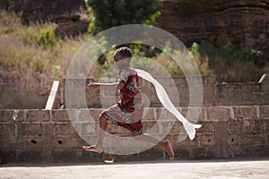 Colourfully Dressed Little African Girl Running With Her White Scarf Flowing In The Wind