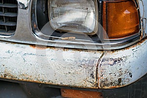 Colse up to decay and rust on the front bumper of an old white truck.