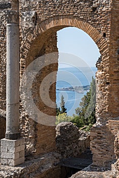 Column and arch at old ruins of ancient Greek theater with sea in background