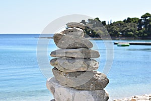 Column made of stones on a beach of Brijuni island and calm blue water of Adriatic sea